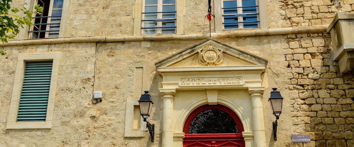 A historic building with a clock tower, red doors, and a sign reading "Hotel de Ville".