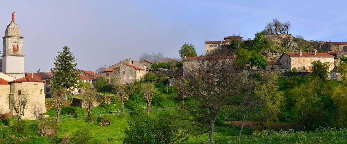 A historic town with stone buildings, a church tower, and lush greenery.
