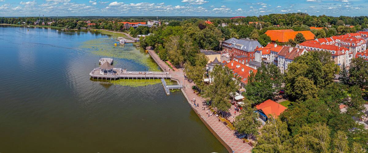 A riverside town with a pier, red-roofed buildings, and a clear blue sky.