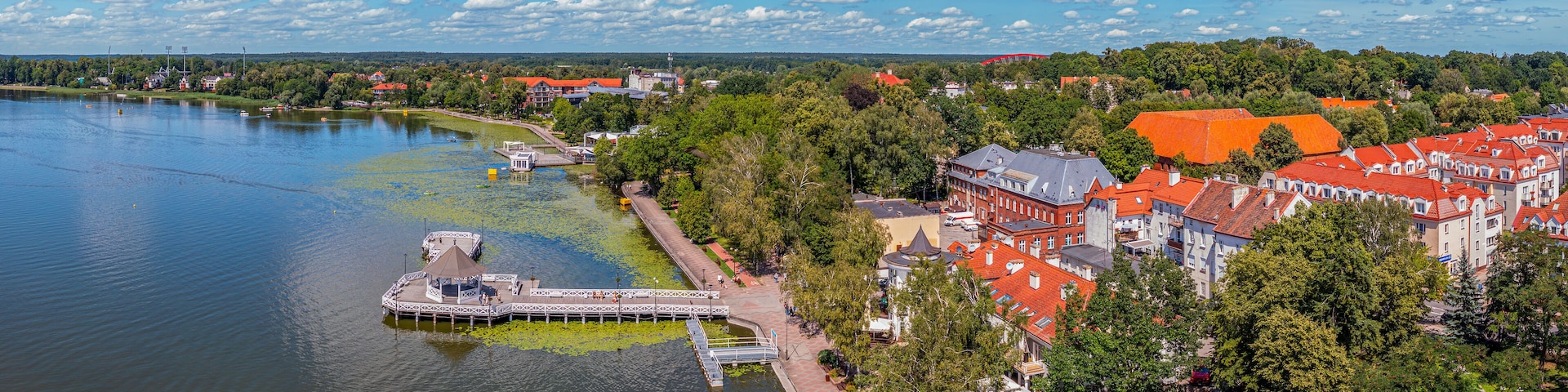 A riverside town with a pier, red-roofed buildings, and a clear blue sky.