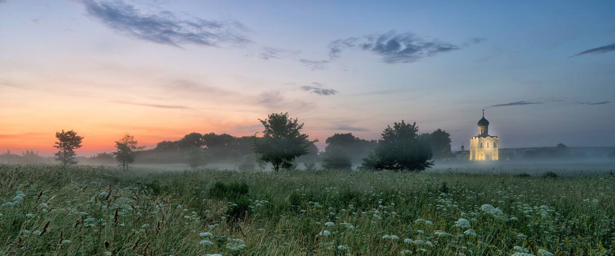 A misty field with a church illuminated in the background.