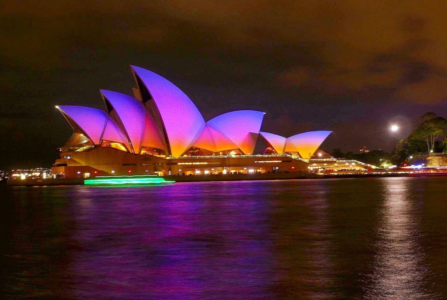 A brightly lit opera house with multiple arched sections and a waterfront backdrop.