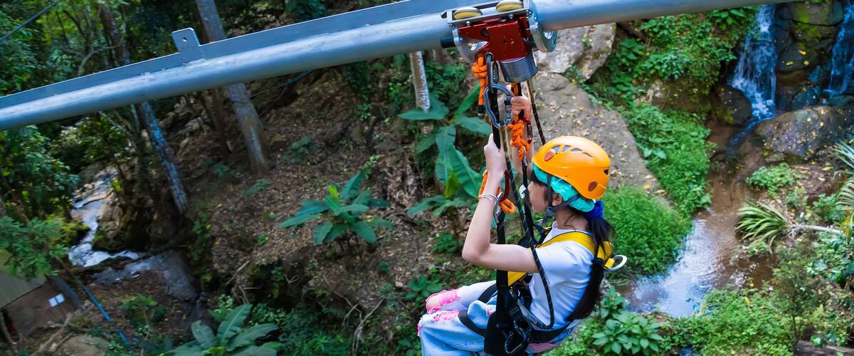 A person zip-lining through a lush, green forest with a waterfall in the background.