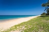 A beach with clear turquoise water, sandy shore, and green vegetation.