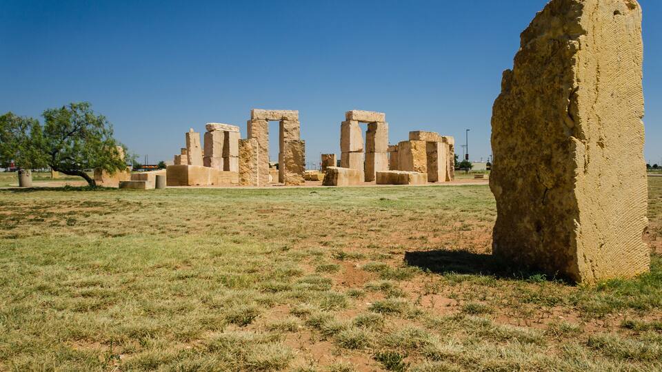 Ancient stone ruins with rectangular doorways and a large standing stone in a grassy field.