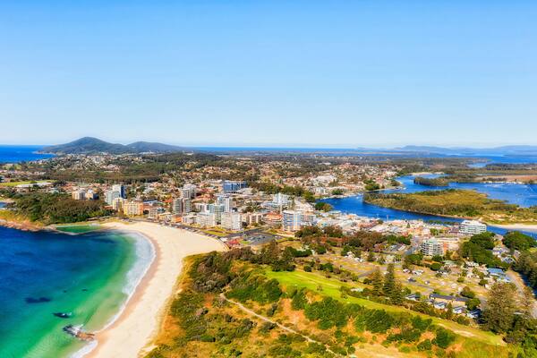 A coastal cityscape with a beach, residential areas, and a mountain in the distance.