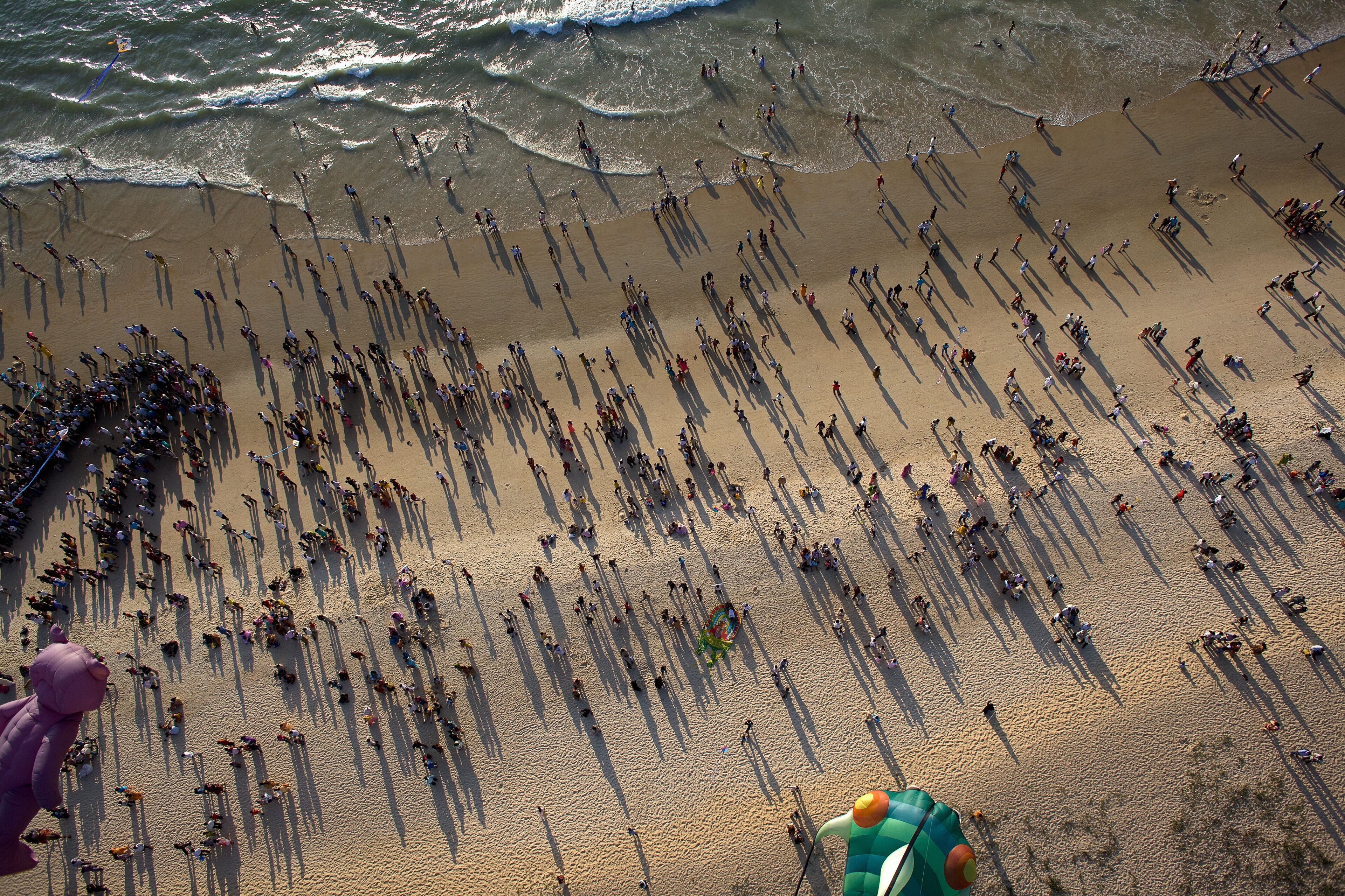 Mangaluru, India - 17 January 2010: Aerial view of sun-drenched sands teeming with figures casting long shadows near the crashing waves of Panambur Beach.