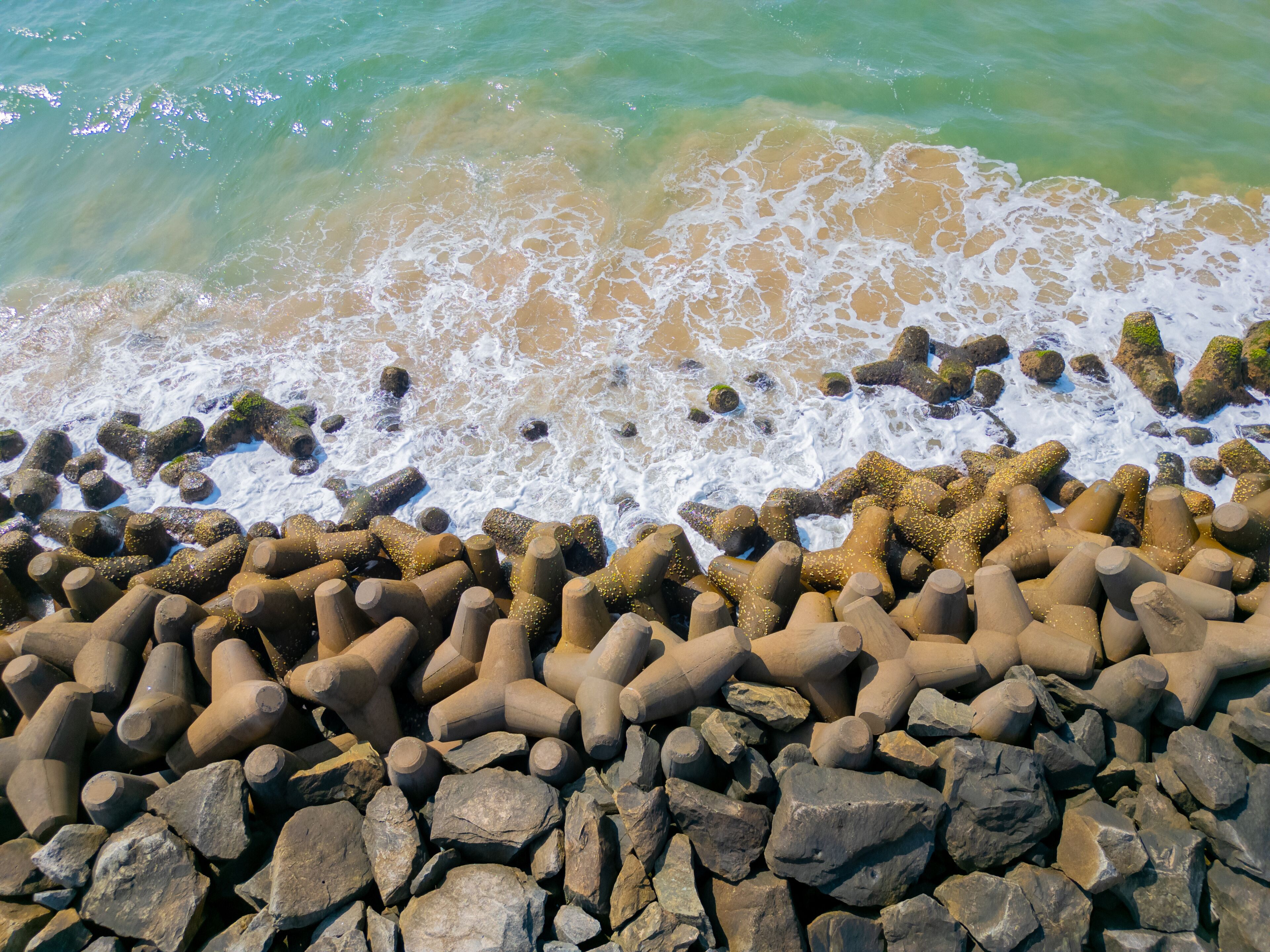 Aerial view of a rocky coastline near Maravanthe Beach, Karnataka, with waves crashing against rugged rocks along the Arabian Sea, creating a dramatic and scenic natural landscape.