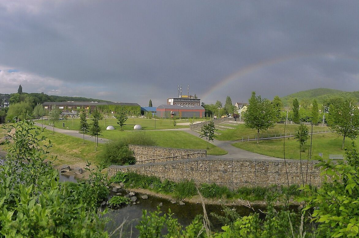 A park with a building, a stone wall, and a rainbow.