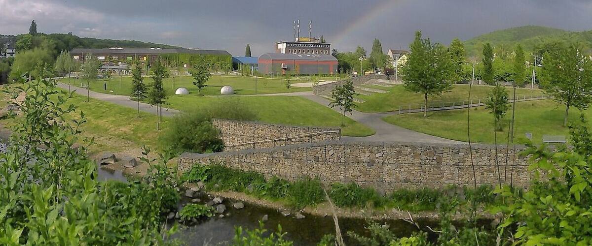 A park with a building, a stone wall, and a rainbow.