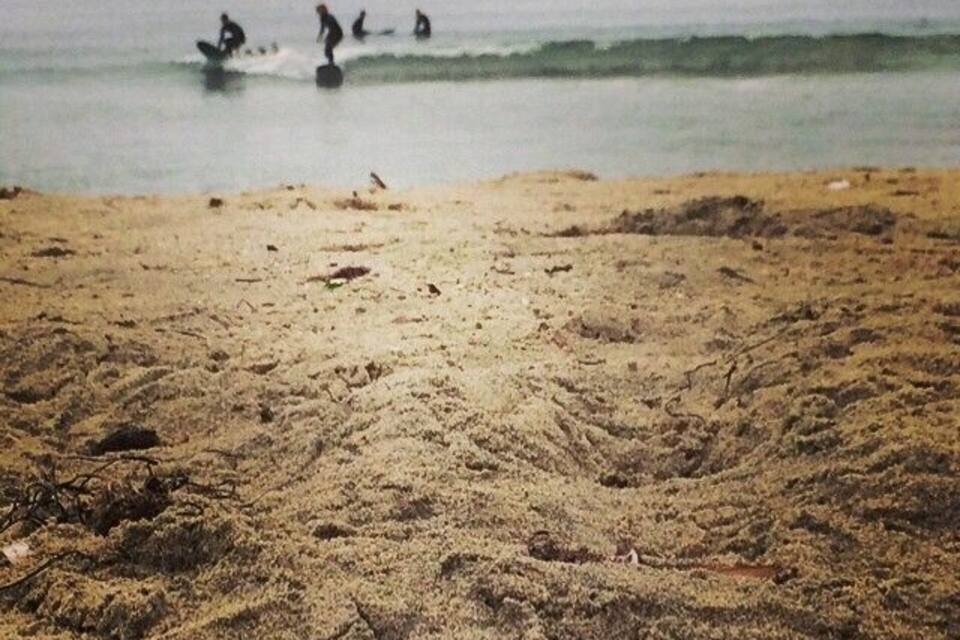 A sandy beach with footprints and a few surfers in the water.