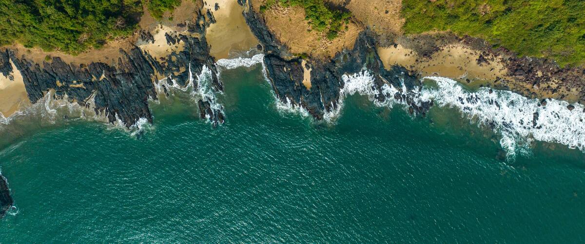 A coastal landscape with a rocky shoreline, sandy beach, and dense green vegetation.