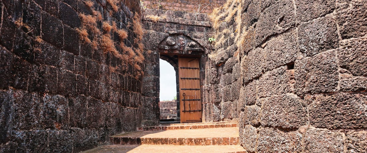 A stone archway leading to a wooden door, flanked by rough stone walls.
