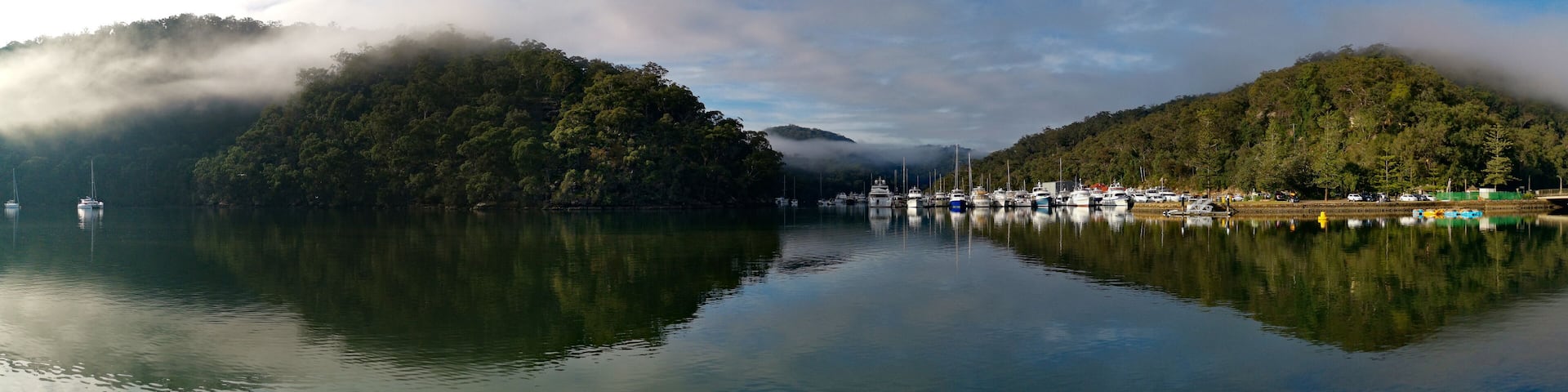 Beautiful morning panoramic view of Cockle creek with reflections of blue sky, light clouds, foggy mountains and trees, Bobbin Head, Ku-ring-gai Chase National Park, New South Wales, Australia