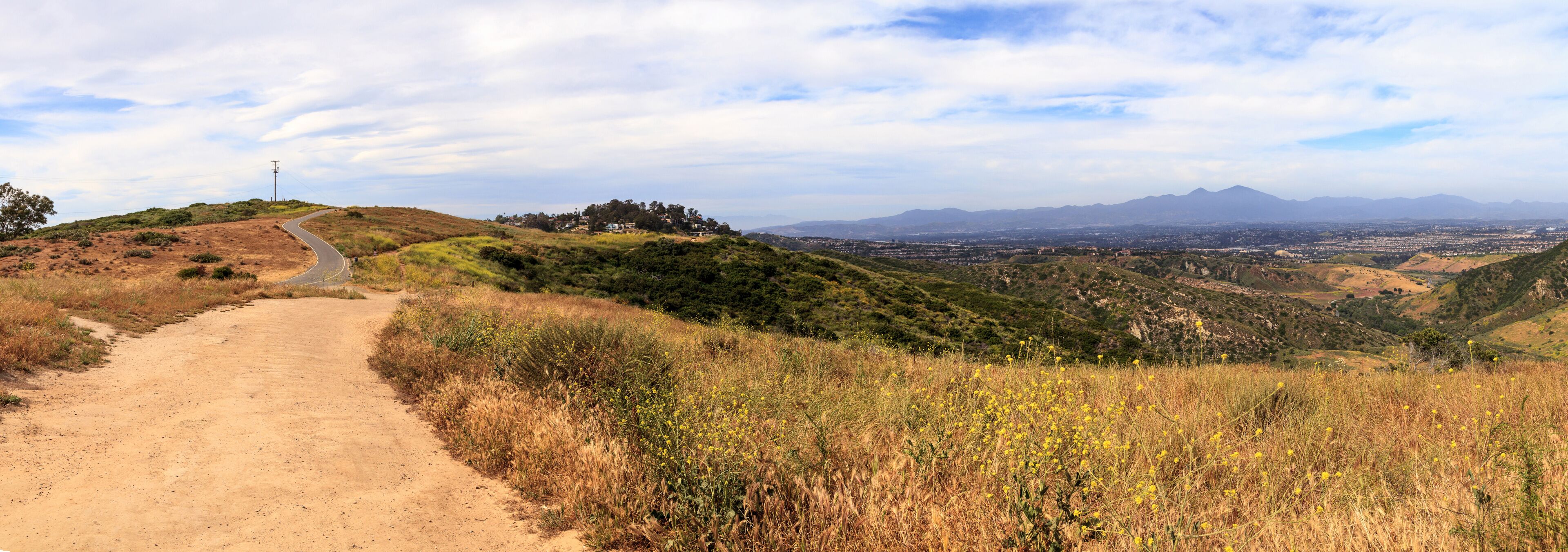 A dirt path leading through a hilly landscape with sparse vegetation and distant mountains.