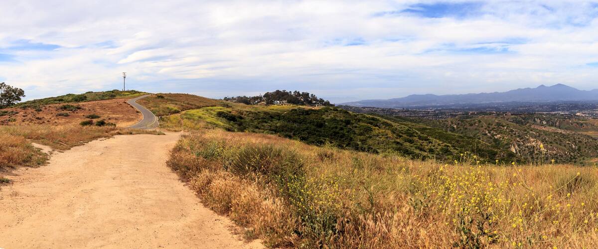 A dirt path leading through a hilly landscape with sparse vegetation and distant mountains.