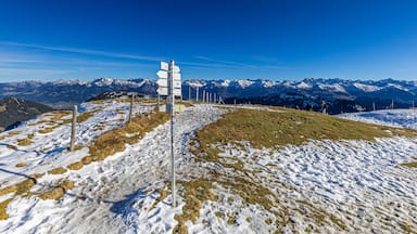 A snow-covered mountain landscape with a signpost and distant snow-capped peaks under a clear blue sky.
