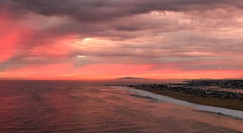 Dramatic red sunset beneath dark storm clouds over the Pacific Ocean and Newport Beach coastline in Southern California, with glowing crimson light stretching across the horizon and reflecting on the