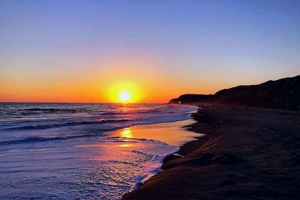 Un coucher de soleil sur une plage, avec des vagues et un ciel dégagé.