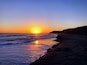 Un coucher de soleil sur une plage, avec des vagues et un ciel dégagé.