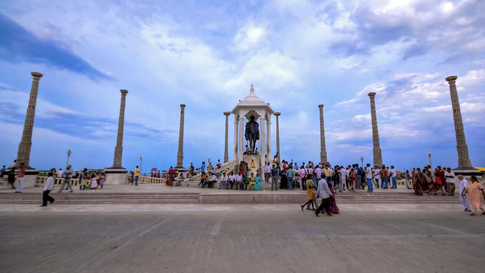 Une vaste place ouverte, avec un monument central entouré de colonnes, sous un ciel partiellement nuageux.