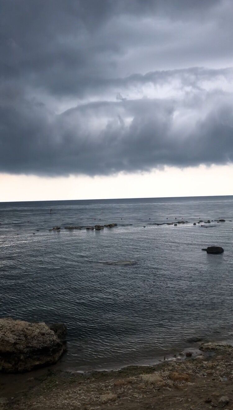 A coastal scene with a rocky shoreline and calm sea under a cloudy sky.