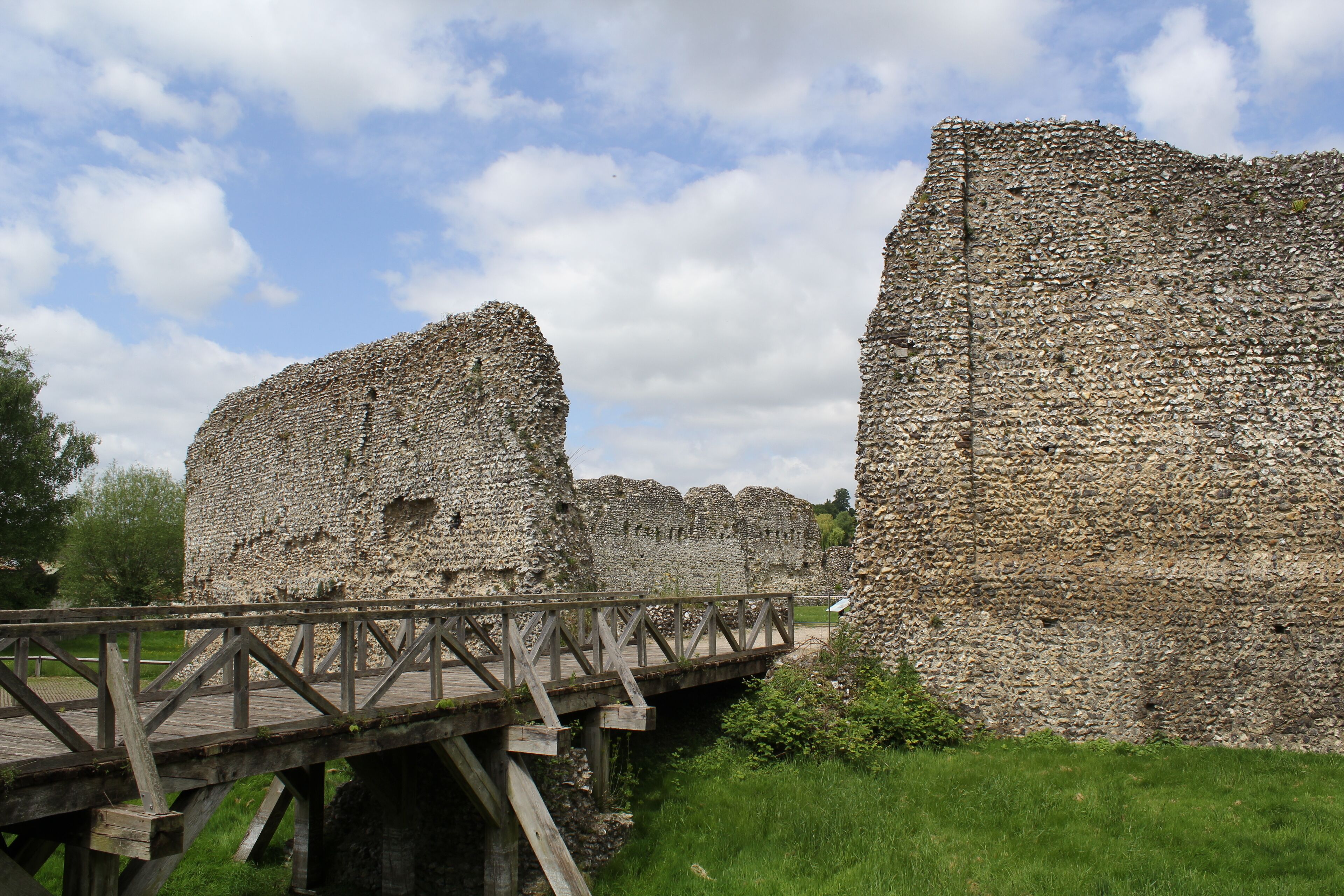 A stone bridge over a moat, leading to a stone wall with a wooden walkway.