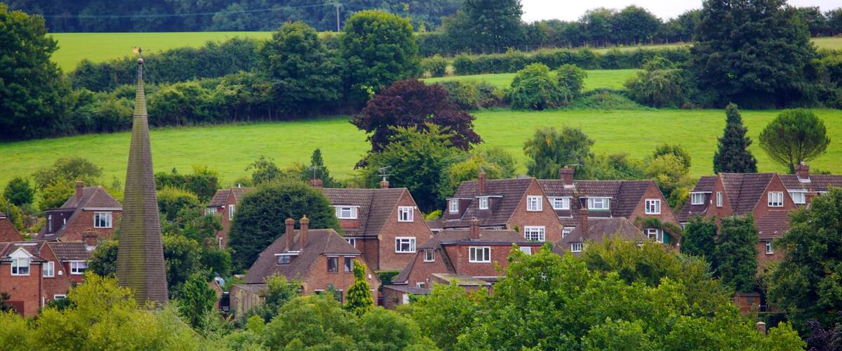 A village with red brick houses, a church spire, and lush green fields.