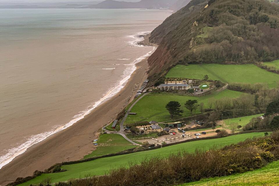A coastal landscape with a beach, a cliff, and a residential area with houses and a road.
