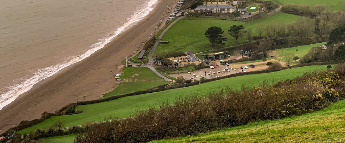 A coastal landscape with a beach, a cliff, and a residential area with houses and a road.