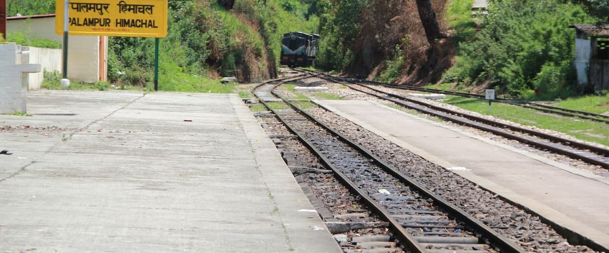 A railway track with a sign reading "Palampur Himachal" in Hindi.