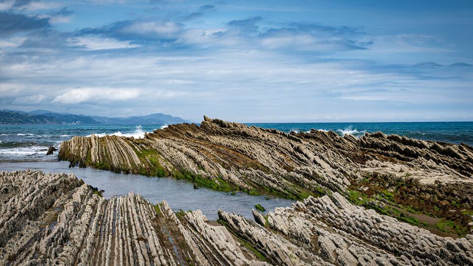 A coastal landscape with layered rock formations and the ocean in the background.