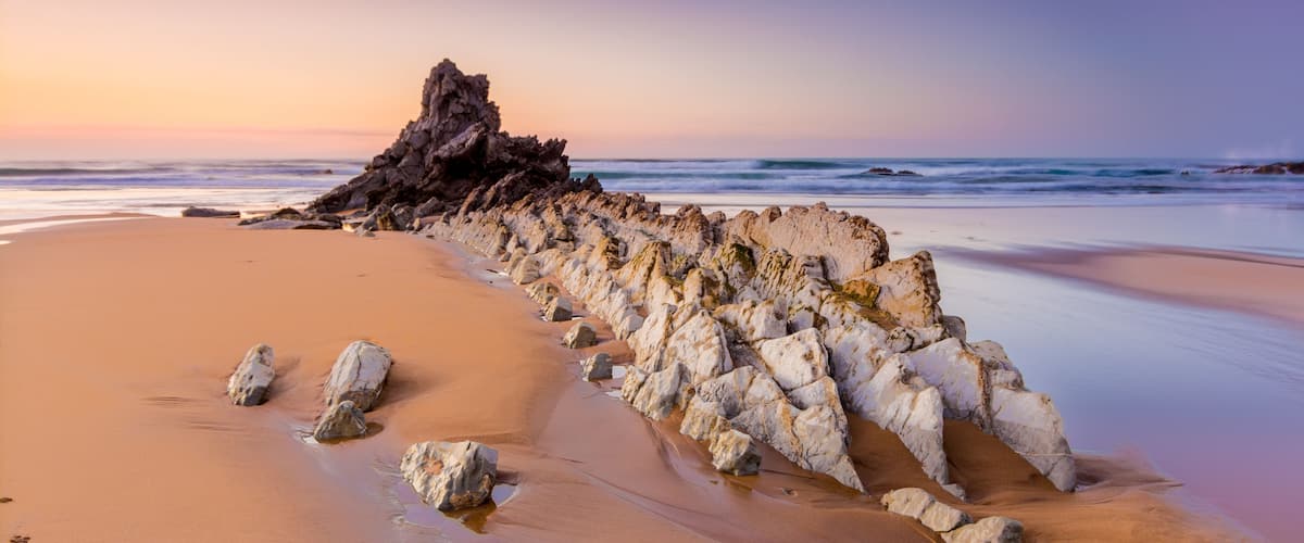 Una playa con una formación rocosa y olas al atardecer.