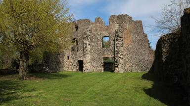 An ancient stone castle with multiple arched doorways and windows, surrounded by a grassy area and trees.
