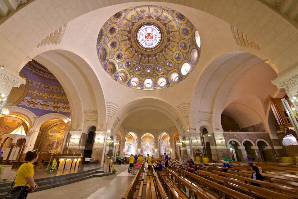 Interior de igreja com uma grande janela circular de vitrais, tetos abobadados e bancos de madeira.