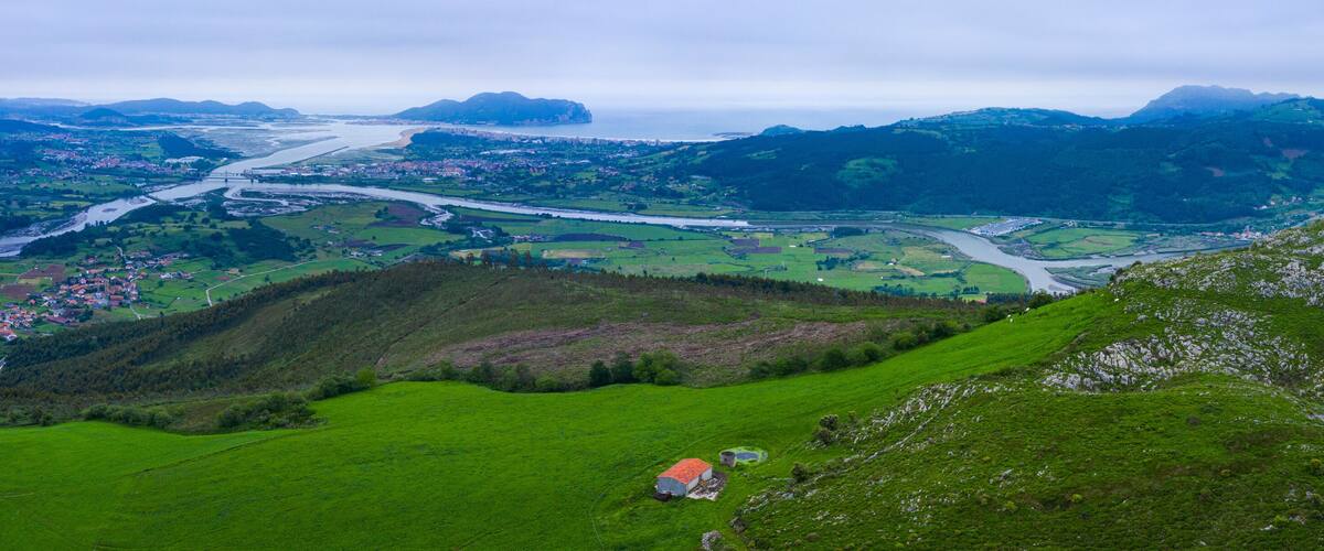 A lush green valley with a river, a bridge, and a small house.