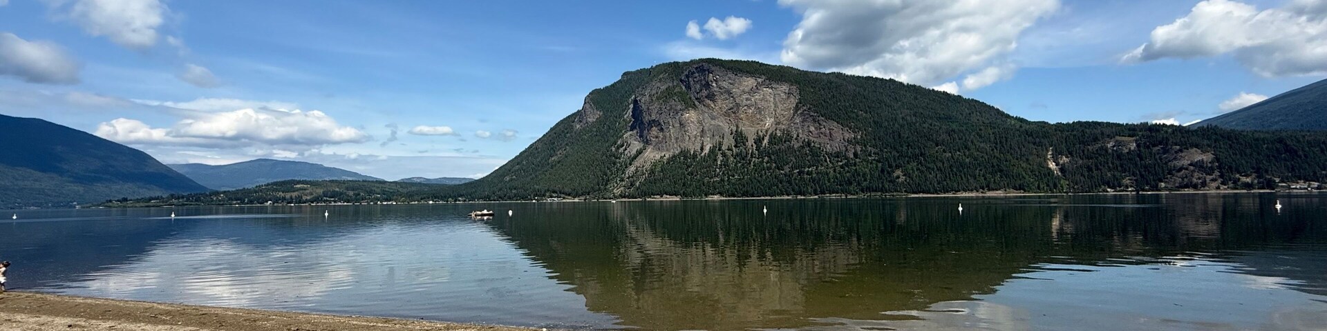 Um lago tranquilo com uma montanha ao fundo e céu claro.
