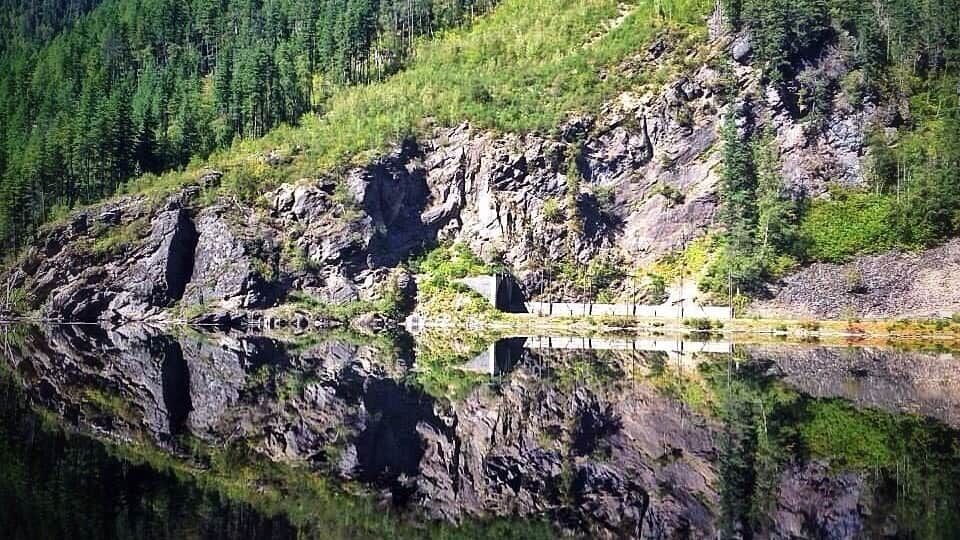 A rocky shoreline with a bridge over calm water, surrounded by dense forest.
