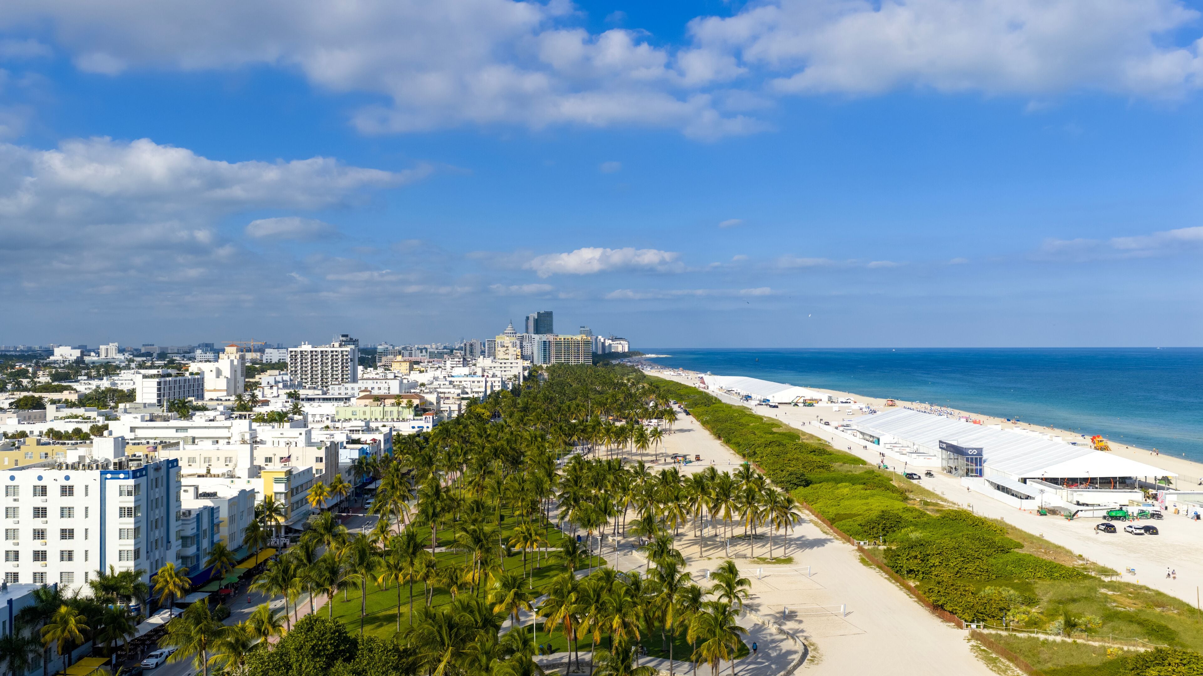 A coastal cityscape with a beach, palm-lined promenade, and high-rise buildings.