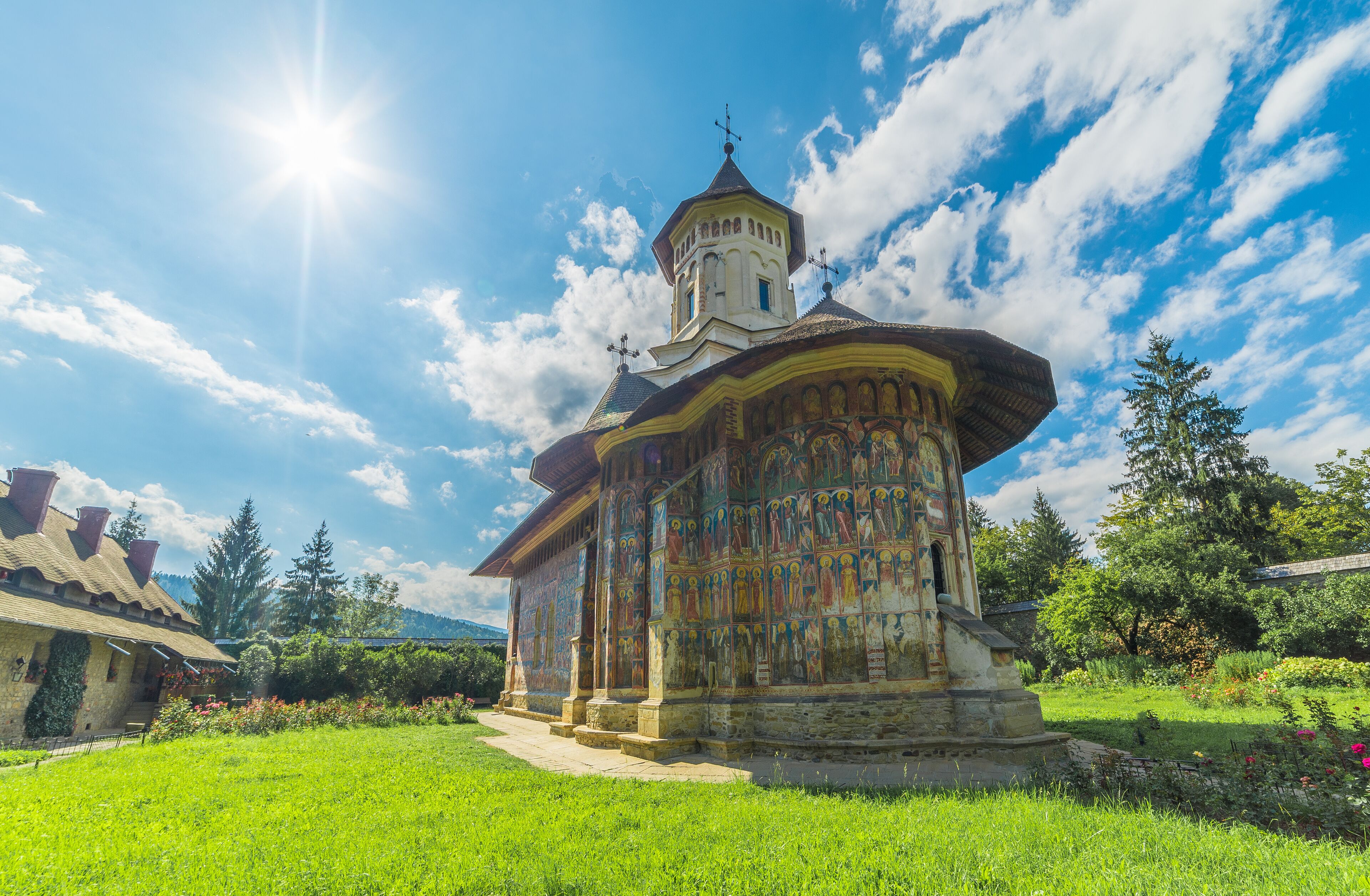 A church with a colorful fresco, surrounded by a lush garden and a clear blue sky.