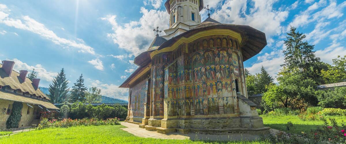 A church with a colorful fresco, surrounded by a lush garden and a clear blue sky.