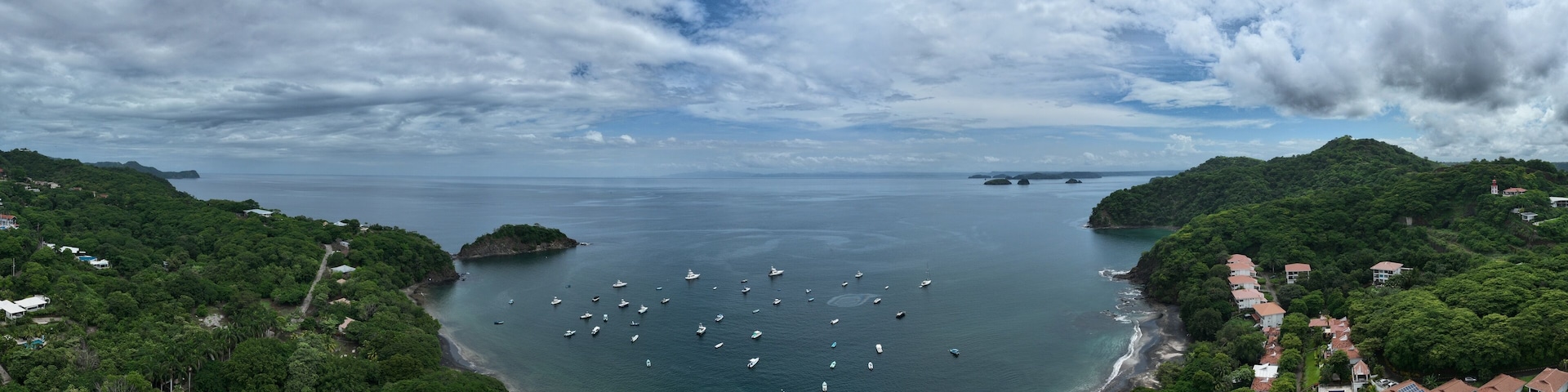 A coastal landscape with dense greenery, a bay filled with boats, and a distant island.