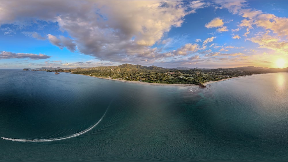 Un paysage côtier avec un ciel dégagé, une mer calme et un soleil se couchant sur une île montagneuse.