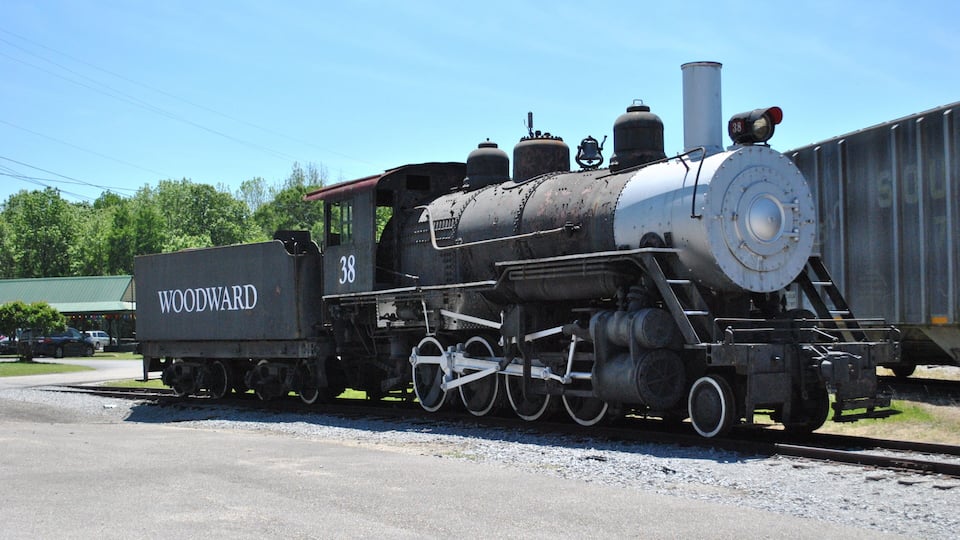 An old steam locomotive with 'WOODWARD' and the number '38' on its side, parked on a railway track.