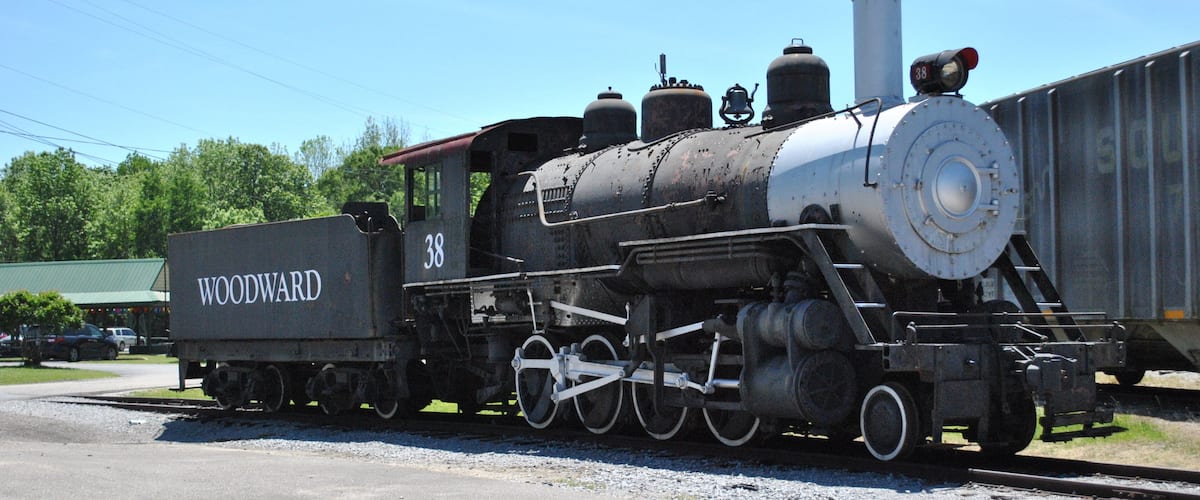 An old steam locomotive with 'WOODWARD' and the number '38' on its side, parked on a railway track.