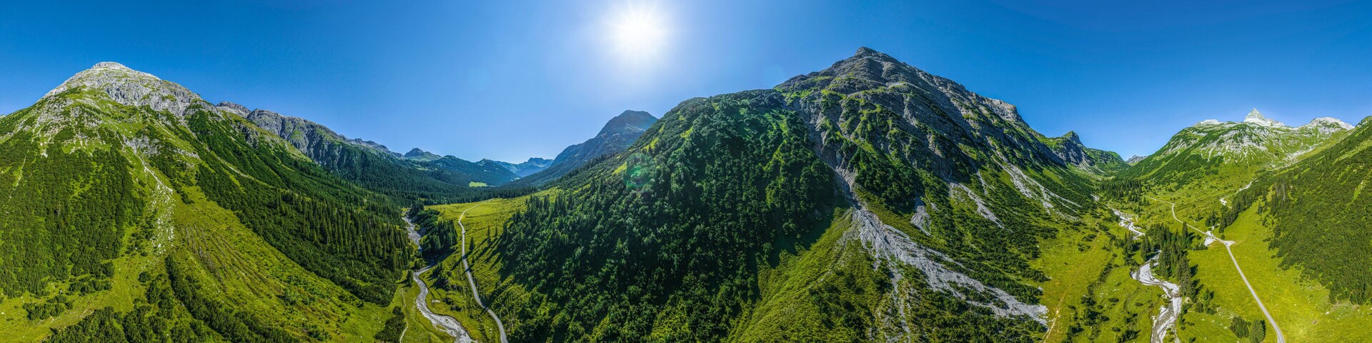 A mountain landscape with a clear sky and a winding road through a valley.