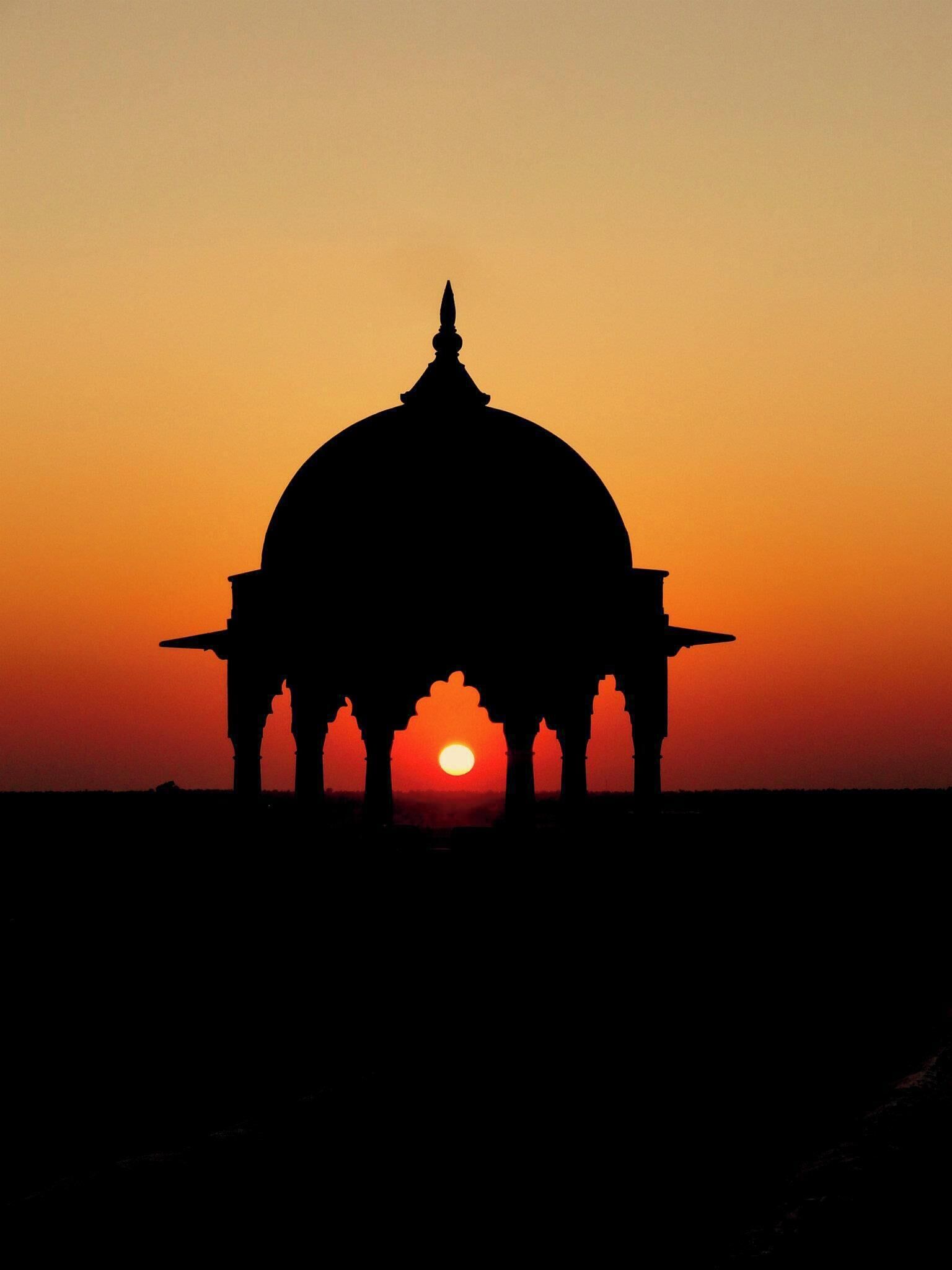 A silhouette of a domed structure against a sunset sky.