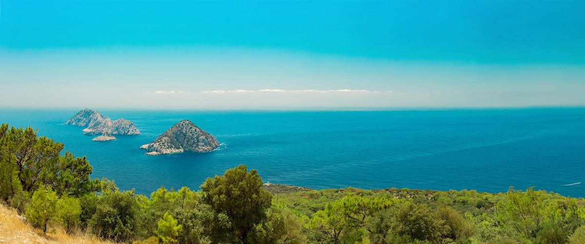 A coastal landscape with three rocky islands and dense green vegetation.