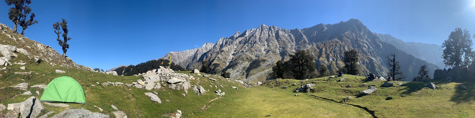 Una carpa verde sobre una ladera cubierta de hierba con terreno rocoso y una montaña al fondo.