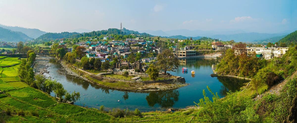A village by a river with terraced fields and a mountain in the background.